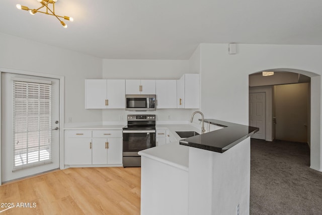 kitchen with a peninsula, arched walkways, a sink, appliances with stainless steel finishes, and white cabinetry