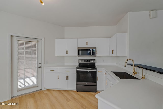 kitchen with a sink, appliances with stainless steel finishes, light countertops, and light wood finished floors