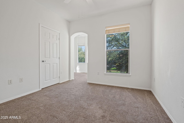 empty room featuring baseboards, arched walkways, and carpet