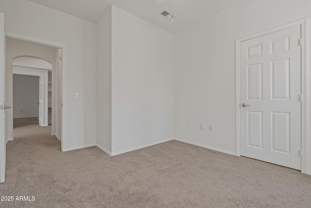 carpeted spare room with visible vents, arched walkways, and baseboards