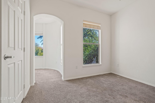 empty room featuring arched walkways, baseboards, and carpet floors