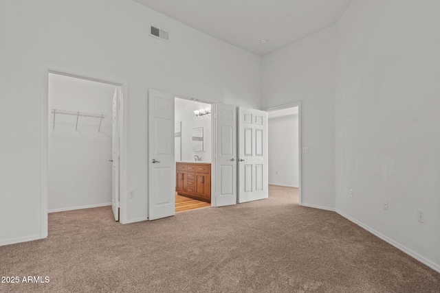 unfurnished bedroom with visible vents, a walk in closet, a closet, baseboards, and light colored carpet