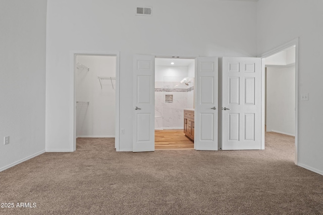 unfurnished bedroom featuring a walk in closet, visible vents, ensuite bath, a closet, and carpet flooring