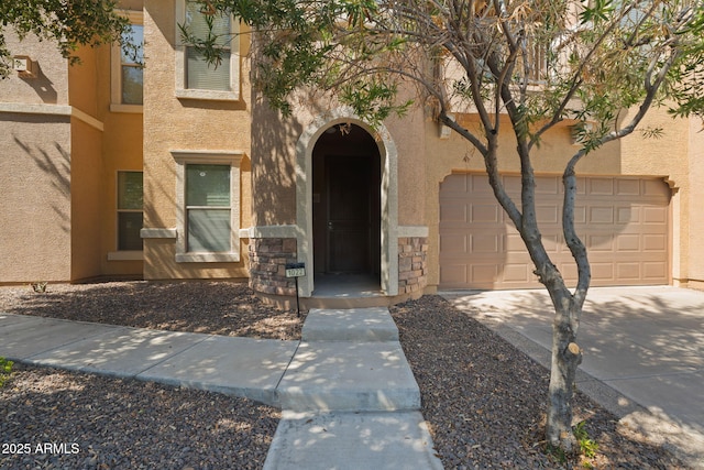 view of exterior entry with stone siding, stucco siding, driveway, and a garage