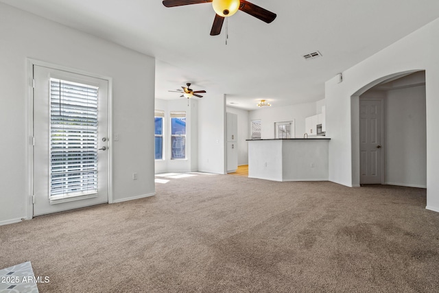 unfurnished living room with visible vents, light colored carpet, arched walkways, and ceiling fan