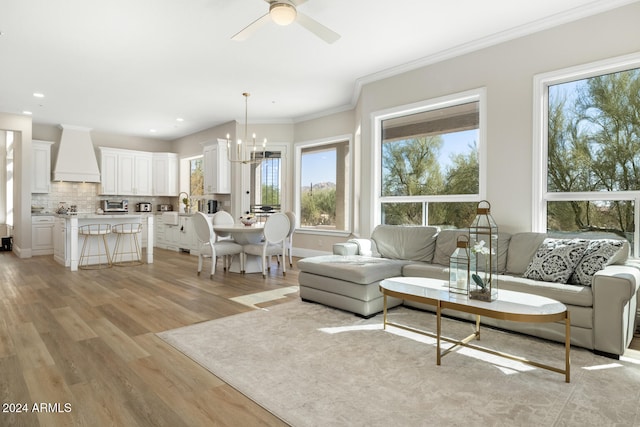 living room with a healthy amount of sunlight, ornamental molding, light hardwood / wood-style flooring, and ceiling fan with notable chandelier