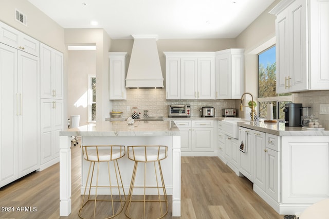 kitchen with light hardwood / wood-style floors, white cabinets, custom range hood, and a center island