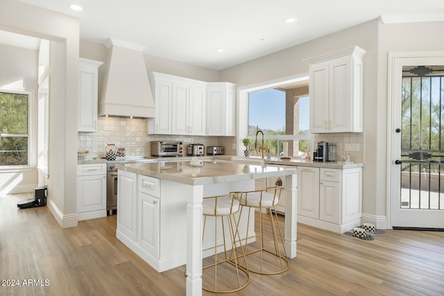 kitchen featuring decorative backsplash, white cabinets, premium range hood, light hardwood / wood-style floors, and a center island