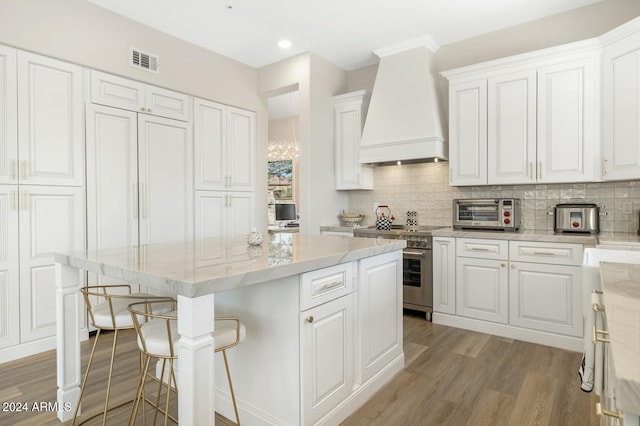 kitchen with white cabinets, a kitchen island, light hardwood / wood-style floors, high end stove, and custom range hood