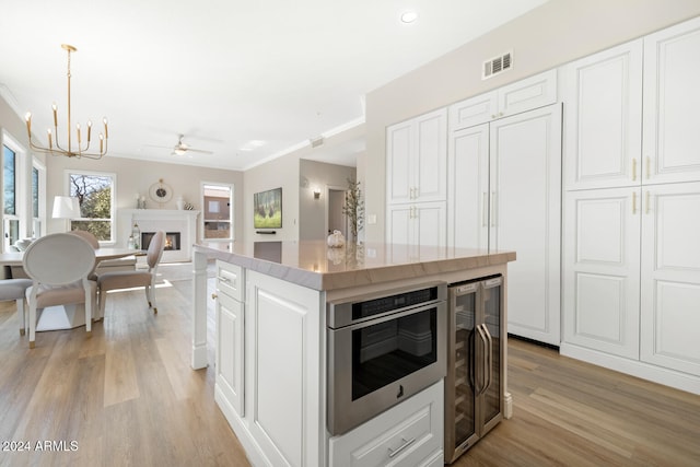 kitchen featuring light hardwood / wood-style flooring, a center island, decorative light fixtures, beverage cooler, and white cabinetry