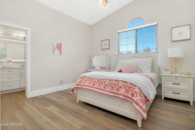 bedroom featuring ensuite bathroom, lofted ceiling, light wood-type flooring, and an inviting chandelier