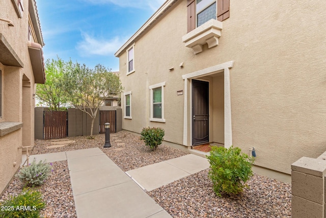 view of exterior entry with a gate, fence, and stucco siding