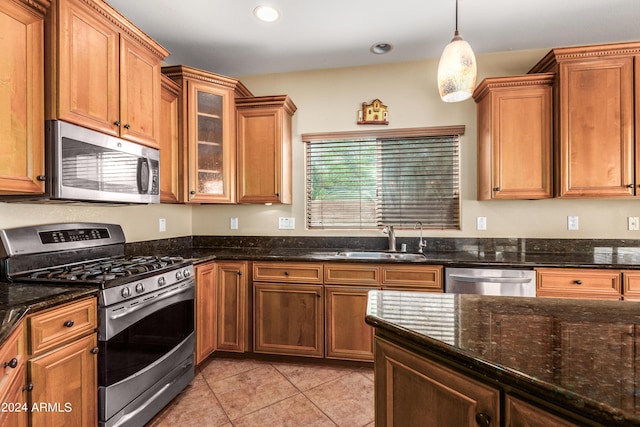 kitchen with light tile patterned floors, brown cabinetry, dark stone counters, stainless steel appliances, and a sink