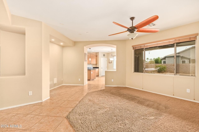 spare room featuring arched walkways, ceiling fan, light tile patterned floors, light carpet, and baseboards