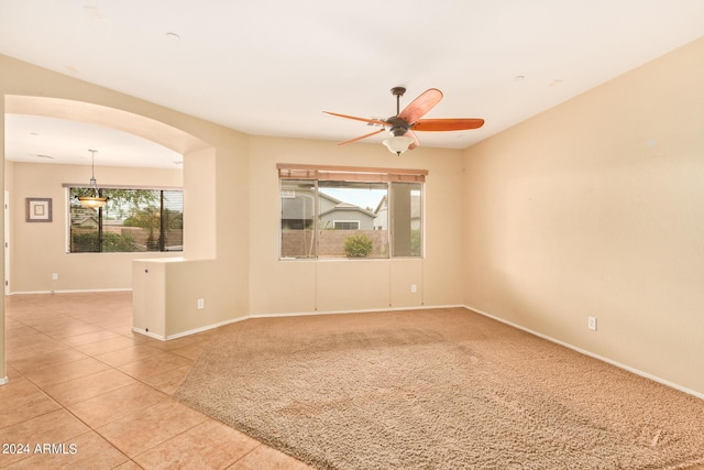 empty room with arched walkways, a ceiling fan, light tile patterned flooring, light carpet, and baseboards