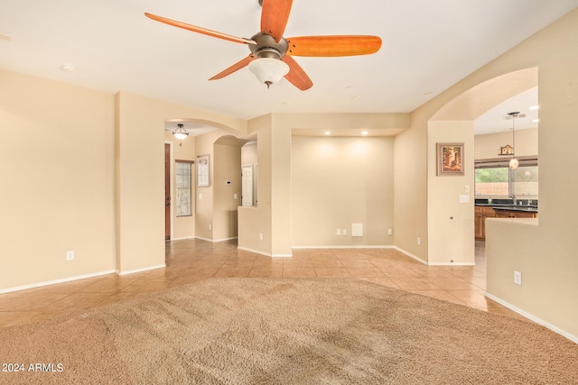 unfurnished room with light carpet, light tile patterned floors, baseboards, arched walkways, and a ceiling fan