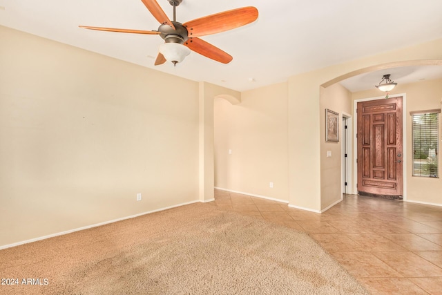 spare room with baseboards, arched walkways, a ceiling fan, light colored carpet, and light tile patterned flooring