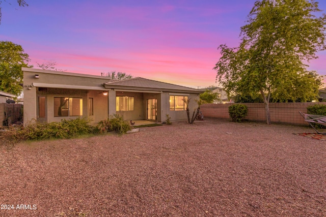 back of house at dusk featuring fence and stucco siding