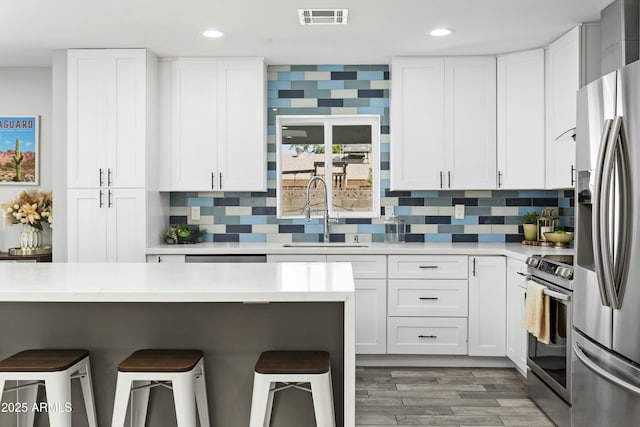 kitchen featuring visible vents, appliances with stainless steel finishes, light countertops, a kitchen bar, and a sink