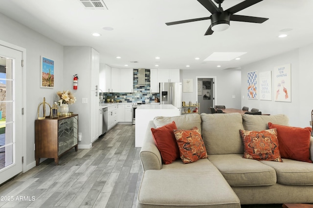 living room featuring recessed lighting, visible vents, light wood finished floors, and a skylight