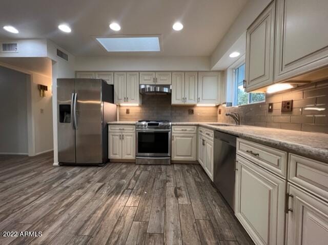 kitchen featuring backsplash, dark wood-type flooring, appliances with stainless steel finishes, and a skylight