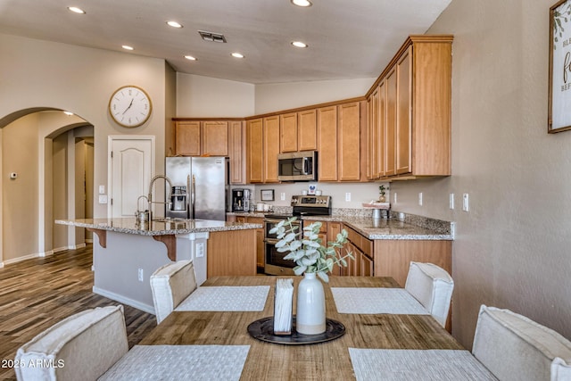 kitchen with lofted ceiling, a breakfast bar area, stainless steel appliances, light stone countertops, and a kitchen island with sink