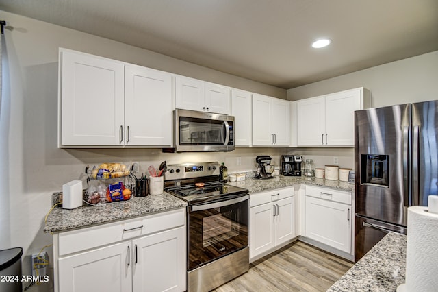 kitchen with white cabinets, light stone countertops, stainless steel appliances, and light hardwood / wood-style flooring