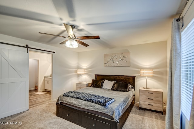 bedroom featuring ceiling fan, a barn door, light colored carpet, and ensuite bath