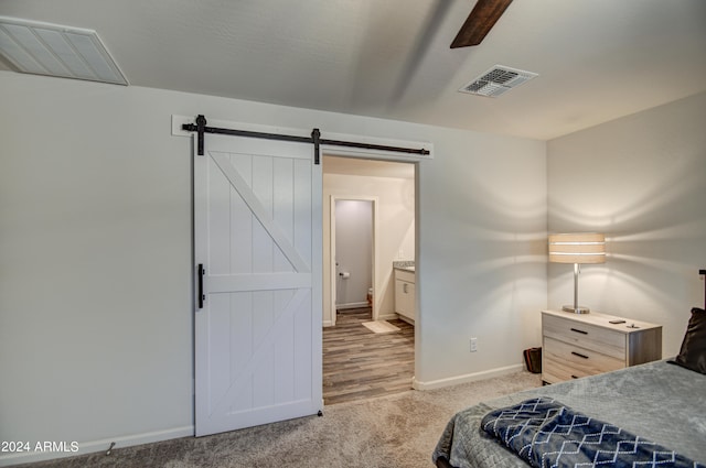 carpeted bedroom with ceiling fan, a barn door, and connected bathroom