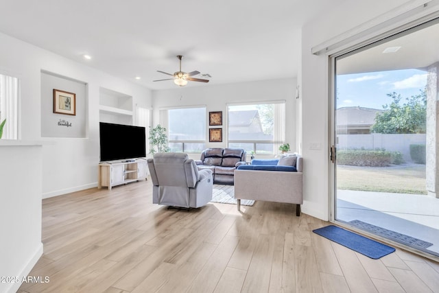 living room with built in shelves, ceiling fan, and light hardwood / wood-style floors