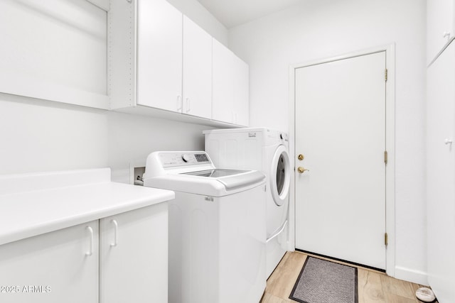 laundry area featuring washer and clothes dryer, light hardwood / wood-style flooring, and cabinets