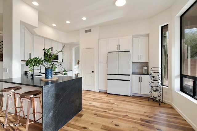 kitchen with white refrigerator, white cabinets, kitchen peninsula, tasteful backsplash, and light wood-type flooring