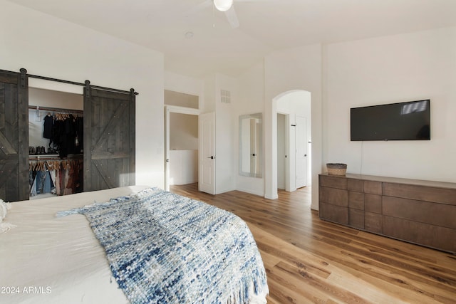 bedroom with hardwood / wood-style floors, a barn door, ceiling fan, and a closet