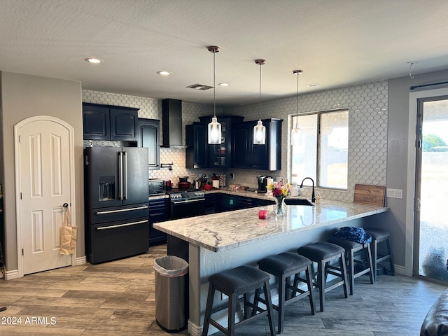 kitchen with a kitchen breakfast bar, wall chimney range hood, hanging light fixtures, kitchen peninsula, and stainless steel appliances