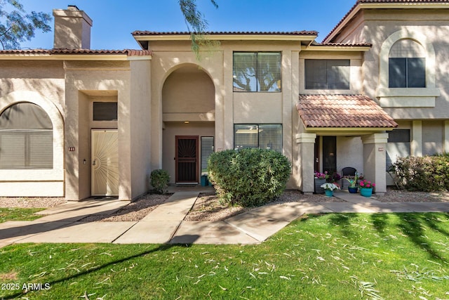 view of front facade with stucco siding, a front yard, a chimney, and a tile roof