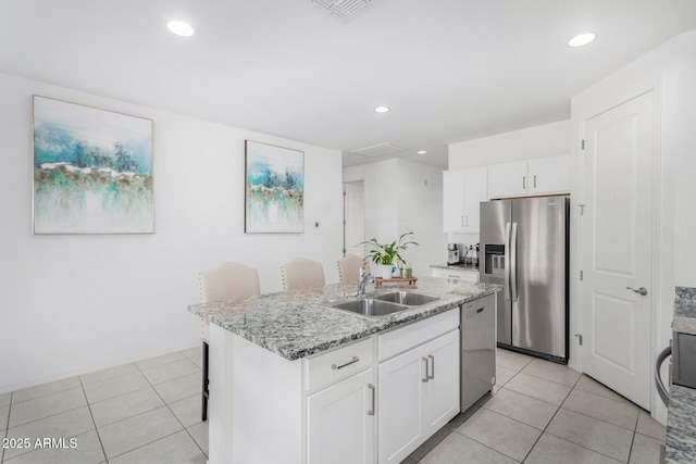 kitchen with light stone counters, a sink, white cabinetry, appliances with stainless steel finishes, and a center island with sink