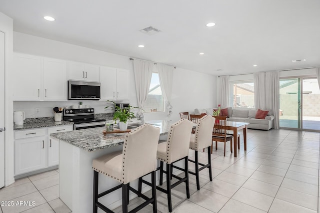 kitchen with visible vents, appliances with stainless steel finishes, open floor plan, white cabinets, and light stone countertops