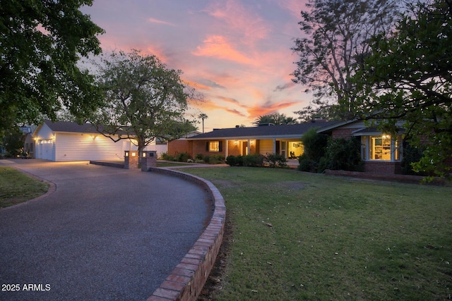 ranch-style house with a garage, a yard, brick siding, and aphalt driveway