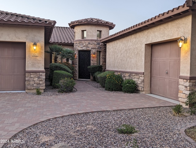 property entrance featuring stone siding, a tiled roof, an attached garage, and stucco siding