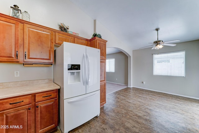 kitchen with white fridge with ice dispenser, a ceiling fan, arched walkways, brown cabinetry, and lofted ceiling
