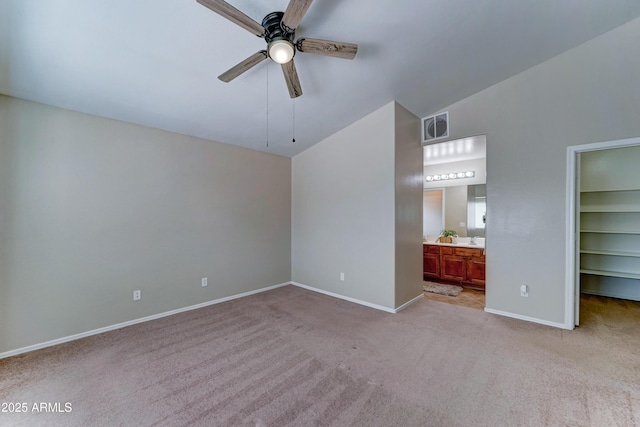 unfurnished bedroom with a spacious closet, light colored carpet, baseboards, vaulted ceiling, and ensuite bathroom