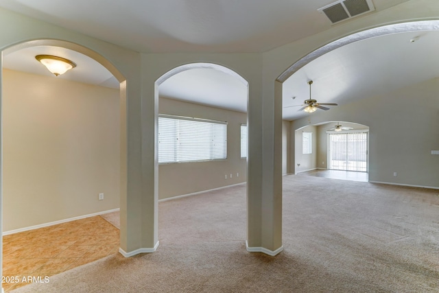 carpeted spare room featuring arched walkways, ceiling fan, and baseboards