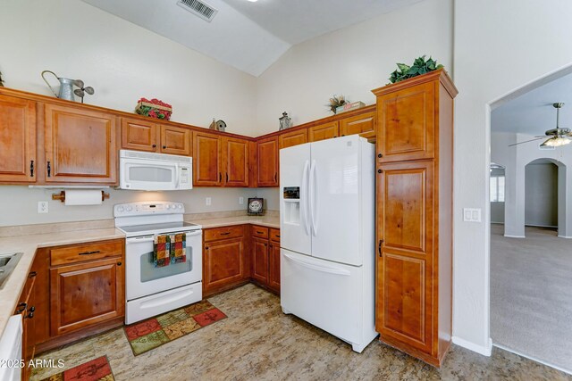kitchen featuring white appliances, arched walkways, lofted ceiling, light countertops, and brown cabinetry