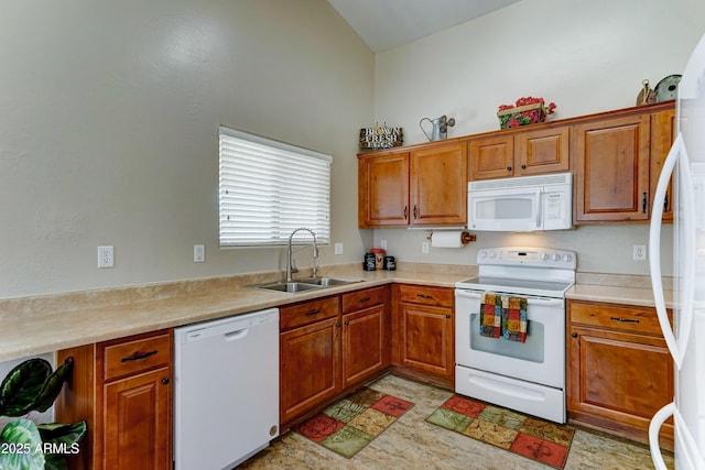 kitchen featuring white appliances, a sink, brown cabinets, and vaulted ceiling