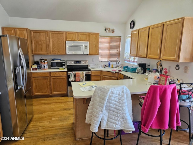 kitchen featuring lofted ceiling, kitchen peninsula, stainless steel appliances, light hardwood / wood-style floors, and sink