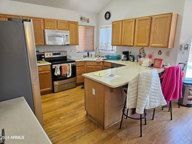 kitchen with kitchen peninsula, light hardwood / wood-style floors, appliances with stainless steel finishes, vaulted ceiling, and sink