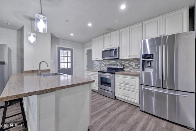 kitchen featuring pendant lighting, sink, stainless steel appliances, white cabinets, and light stone counters