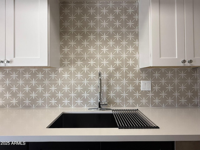 kitchen view of a sink, light countertops, and white cabinetry
