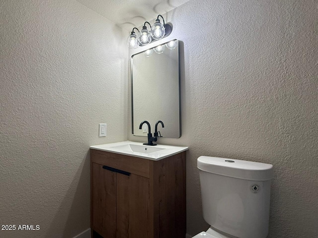 bathroom with vanity, toilet, and a textured wall