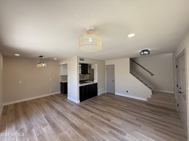 unfurnished living room with stairs, light wood-type flooring, baseboards, and recessed lighting